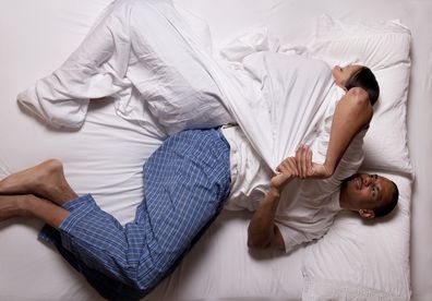 Photograph of an attractive young couple taken from directly above a bed struggling with fair coverage; woman is sleeping soundly and wrapped tightly in all the covers and man is obviously frustrated and trying to pull some of the covers over him; copy space