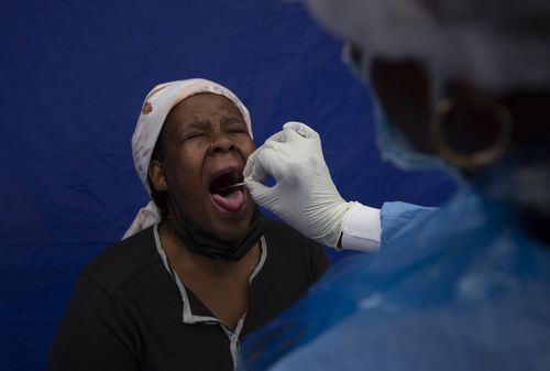 A throat swab is taken from a patient to test for COVID-19 at a facility in Soweto, South Africa, Wednesday Dec. 2, 2021.  