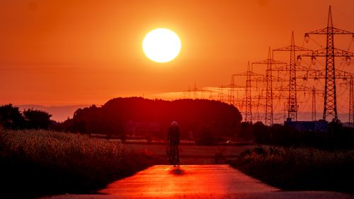 A man rides his bike on a small road with a sunset in the distance