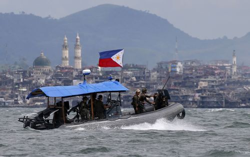 In this 2017 photo, Philippine Navy commandos ride on a gunboat as it patrols the periphery of Lake Lanao. Smoke rises from the main battle area where pro-Islamic group militants made a final stand amid a massive military offensive of Marawi city in southern Philippines.