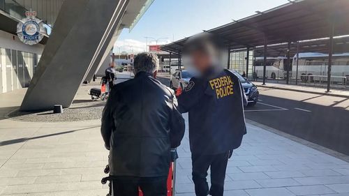 A man from SMEC International Pty is led away by an AFP officer.