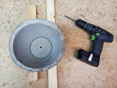 Hole drilled in concrete plant pot during DIY project.