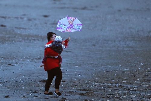 A woman struggles to hold a child and umbrella on Dollymount strand in Dublin. (AAP)