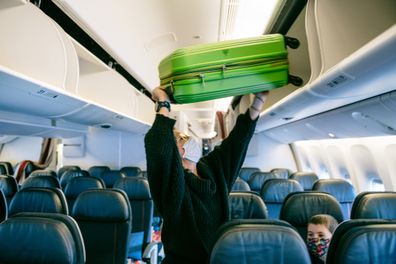 Mother storing carry on luggage on airplane overhead bin
