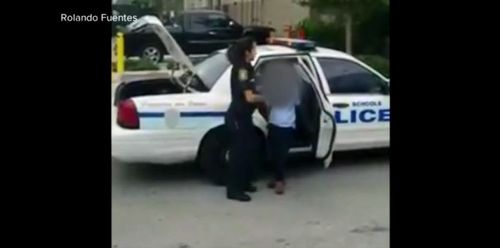 He steps out of a police patrol car and is guided by a police officer into Miami Children's Hospital.