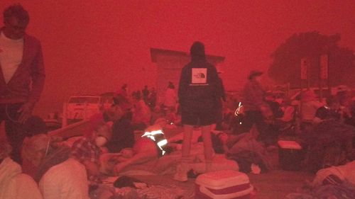 People are pictured on Mallacoota beach, ready to escape into the water if the bushfire moves into the town.