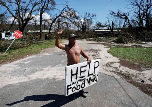 Michael Williams, 70, waves to passing motorists while looking for food and water as downed trees prevent him from driving out of his damaged home with his family in the aftermath of Hurricane Michael in Springfield, Florida.