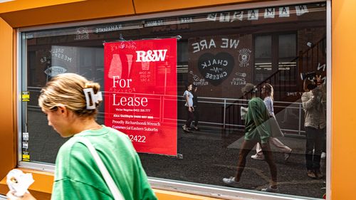 A woman walks past a for lease sign. 