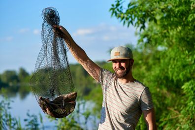 Adult fisherman holding a tank with a bog catch. Happy after a successful fishing. Sport and hobby concept.