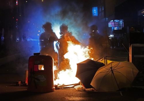 Journalists stand next to fire set by protesters at a main street in Hong Kong.