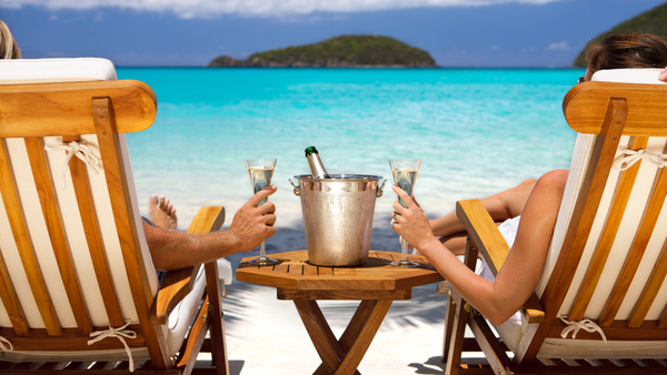 Couple drinking champagne in sun chairs on a beach | Honeymoon holiday couple