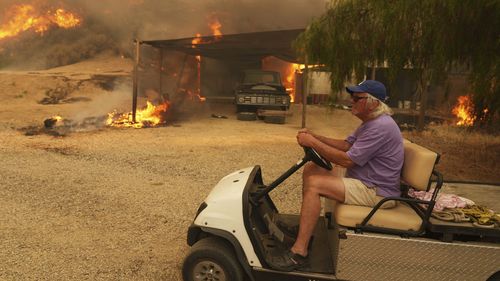 A resident rides a golf cart as he exits his property while the Canyon Fire burns in Hasley Canyon, California.