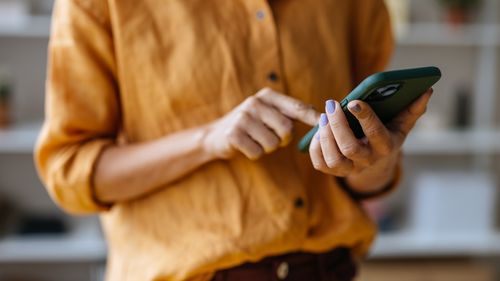 A close up view of an unrecognizable Caucasian entrepreneur texting on her smartphone while standing indoors.
