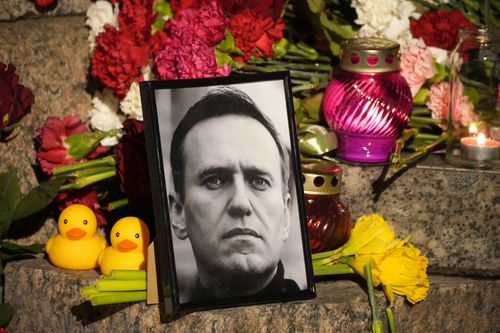 Un portrait du chef de l'opposition russe Alexei Navalny, des fleurs et des bougies sont déposées sur le sol alors que les gens se rassemblent pour rendre un dernier hommage à Alexei Navalny au Mémorial des victimes de la répression politique à Saint-Pétersbourg, en Russie, le vendredi 16 février 2024.