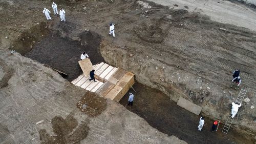Workers wearing personal protective equipment bury bodies in a trench on Hart Island in New York.