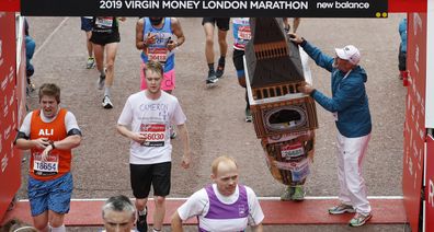 Mr Bates is helped by an official as he attempts to get past the finishing line, during the 39th London Marathon in London, Sunday, April 28, 2019. 