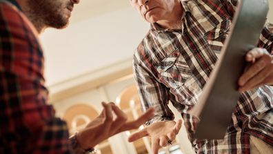 Angry mature man communicating with his younger man about paperwork.