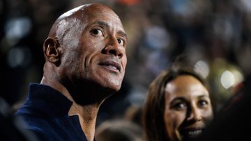 Dwayne &#x27;The Rock&#x27; Johnson stands on the sideline in a football game.