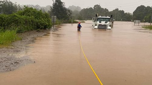 An SES worker secures himself to a rope as he enters floodwaters to inspect a trapped truck. 