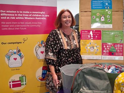 Founder of Care Bags, Sarah Clark, standing in front of a table stacked with backpack care packages.