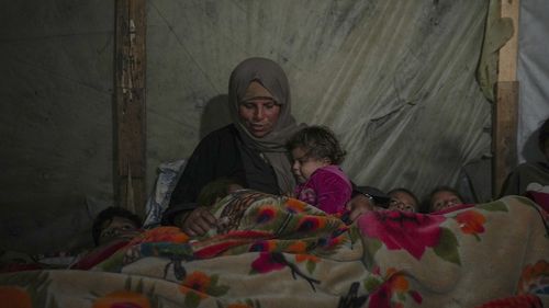 Reda Abu Zarada wraps herself and her grandchildren in blankets as they prepare to sleep in their tent at a camp in Khan Younis, Gaza Strip, Thursday Dec. 19, 2024. (AP Photo/Abdel Kareem Hana)