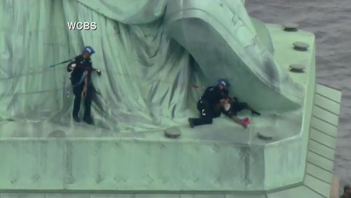 The officers have grabbed the woman and are pulling her down from the base of the statue. Picture: Supplied