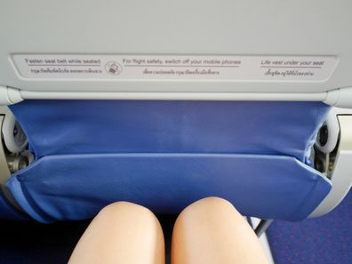 Woman's legs sitting in a plane with warning sign on the front seat legroom
