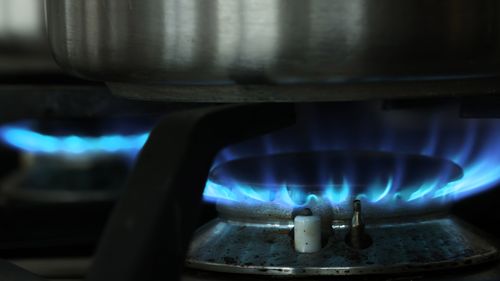 A gas flame burns under a pot on a gas stove top.