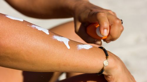 Close up on woman applying sun cream on her arm with a spray at the beach on a warm, sunny day. Sunscreen protection, skin cancer concept