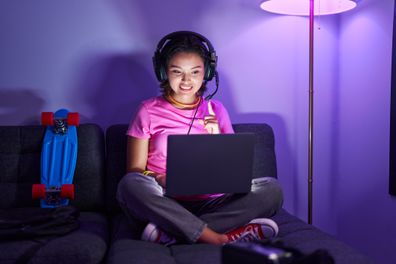 Hispanic young woman playing video games sitting on the sofa smiling happy pointing with hand and finger