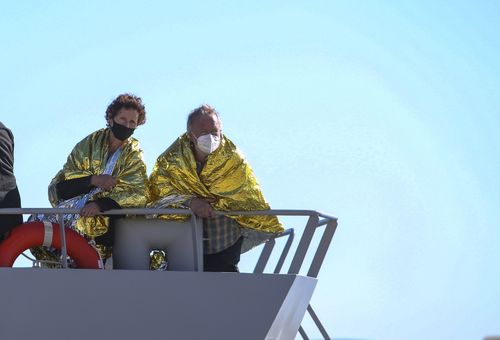 A man and a woman covered with a thermal blankets look out from Greek Navy ship as they arrive at the port of Corfu island, northwestern Greece, following their evacuation from a ferry, Friday, Feb. 18, 2022