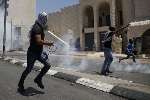 A Palestinian throws back a tear gas grenade against Israeli troops. Picture: EPA