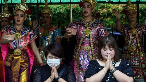 Chinese tourists pray in front of Thai dancers