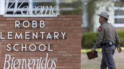 A state trooper walks past the Robb Elementary School sign in Uvalde, Texas, following a deadly shooting at the school.