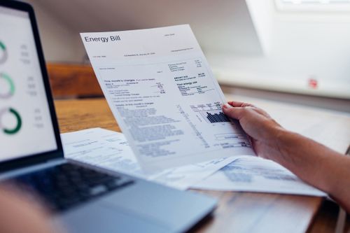 Una persona controlla la propria bolletta energetica mentre utilizza un laptop a casa. Il documento include vari addebiti e informazioni sull'utilizzo dell'elettricità.