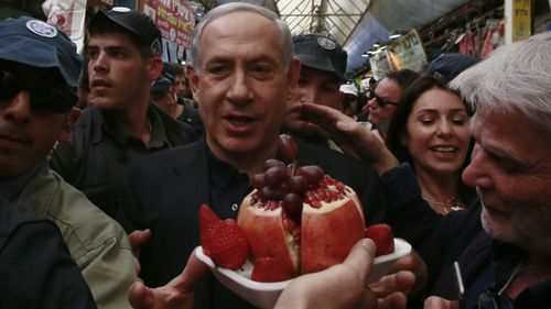 Surrounded by body guards, Israeli Prime Minister and head of the Likud party Benjamin Netanyahu (C) receives fruits from a vendor as he visits the Jerusalem outdoors Mahane Yehuda market