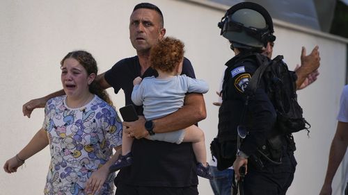 Israeli police officers evacuate a family from a site hit by a rocket fired from the Gaza Strip, in Ashkelon, southern Israel, Saturday, Oct. 7, 2023.  