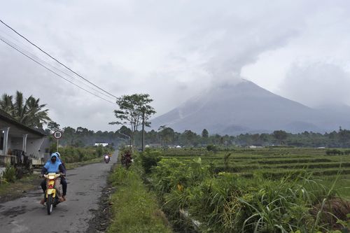 Motorists ride on a village road as Mount Semeru is seen spewing volcanic smoke in Lumajang, East Java, Indonesia, Sunday, Jan. 17, 2021