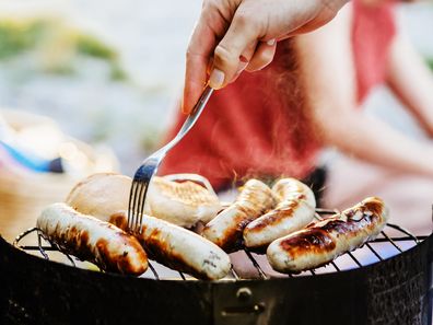 A close up of sausages being cooked on a barbecue by the lake.