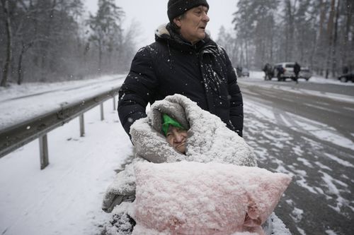 Une femme âgée est recouverte de neige alors qu'elle est assise dans un fauteuil roulant après avoir été évacuée d'Irpin, à la périphérie de Kiev, en Ukraine, le mardi 8 mars 2022. 