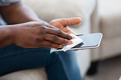 Man Disinfecting Smartphone Screen With Antibacterial Wipe Before Use At Home, Cropped Image, Closeup