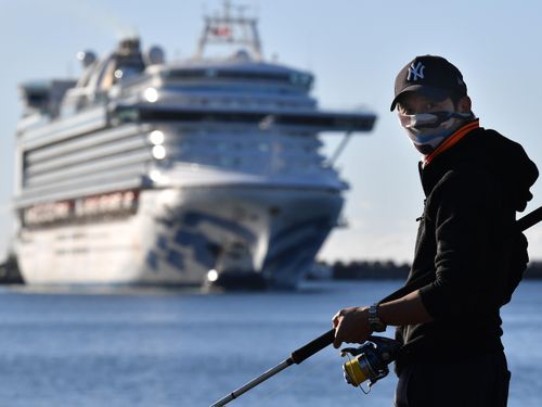 A fisherman wearing a face mask looks on as the Ruby Princess, with crew only onboard, docks at Port Kembla, Wollongong.