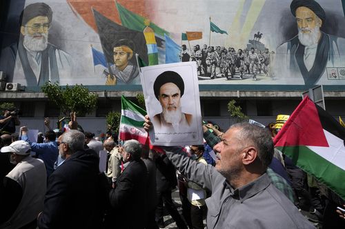 Adoradores iranianos passam por um mural representando o falecido fundador revolucionário, Aiatolá Khomeini, à direita, o Líder Supremo, Aiatolá Ali Khamenei, à esquerda, e a força paramilitar Basij, enquanto seguram uma placa do Aiatolá Khomeini e bandeiras iranianas e palestinas em um comício anti-Israel após suas orações de sexta-feira em Teerã, Irã, sexta-feira, 19 de abril de 2024.