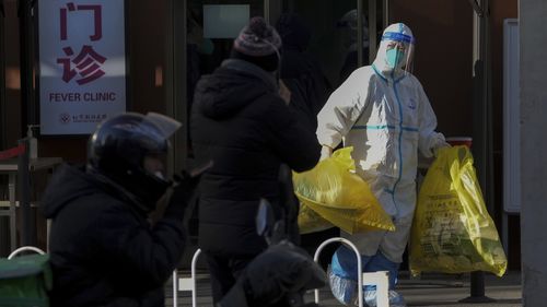 A medical worker in protective gear carries yellow bags of medical waste from a fever clinic in Beijing, Monday, Dec. 19, 2022. 