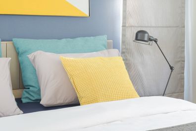 Yellow and green pillow on bed with black foldable lamp on bedside table in modern interior bedroom