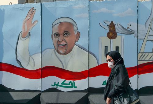 A woman walks past a mural depicting Pope Francis on a concrete wall placed by Iraqi security forces to surround the Our Lady of Salvation Church during preparations for the Pope's visit in Baghdad, Iraq, Monday, March 1, 2021