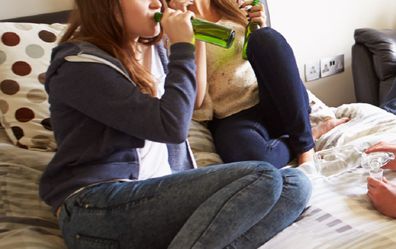 Teenagers drinking alcohol in a bedroom