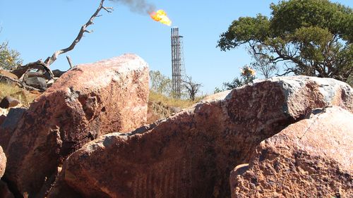 Flare tower of Woodside's Pluto LNG plant in WA with an Indigenous rock engraving of an echidna in the foreground.
