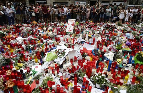 People stand next to candles and flowers placed on the ground after a terror attack that killed 14 people and wounded over 120 in Barcelona, Spain. (AP)