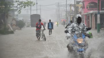 Haitian people travel in a flooded street through the rain during a tropical storm in the commune of Les Cayes, Haiti, on October 21, 2016. (AFP)